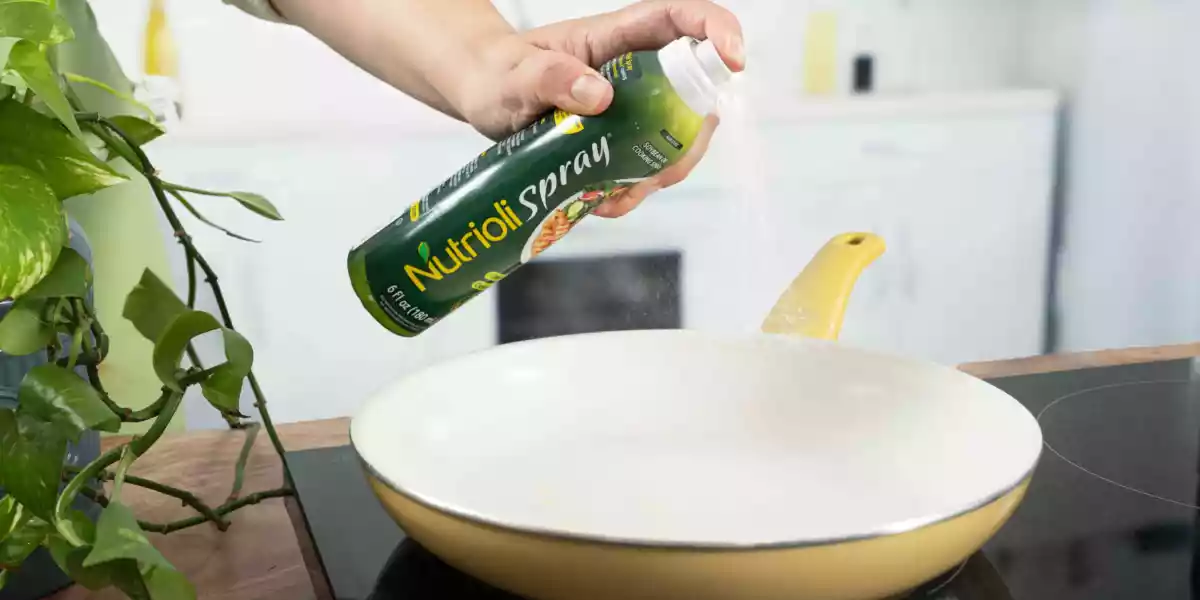 A person sprays oil spray on a frying pan